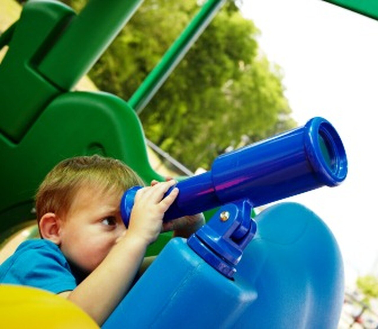 Young child looking through blue play telescope on colorful green and blue playground equipment outdoors
