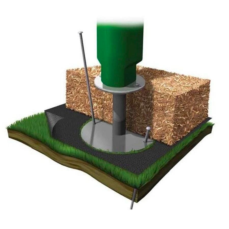 Green metal ground spike with base plate anchored in soil and grass, surrounded by wood mulch block cross-section