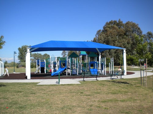 Blue hip roof shade structure with four white posts covering playground equipment in a park setting