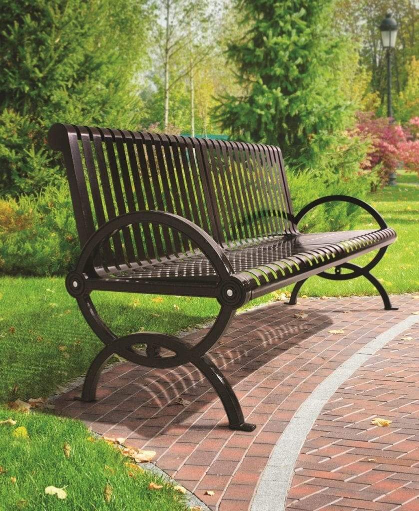 Dark metal outdoor bench with vertical slats and curved armrests on brick pathway in green park setting