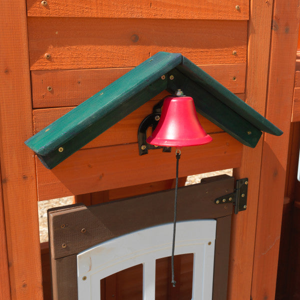 Red pull-string bell mounted under green awning on orange wooden playset wall above brown and white door