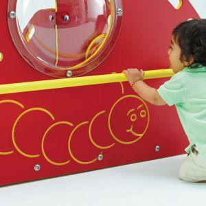 Toddler engaging with red playground panel featuring yellow caterpillar design and clear bubble window on soft play structure