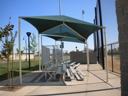 Slanted hip shade structure with four posts covering metal bleachers at a baseball field
