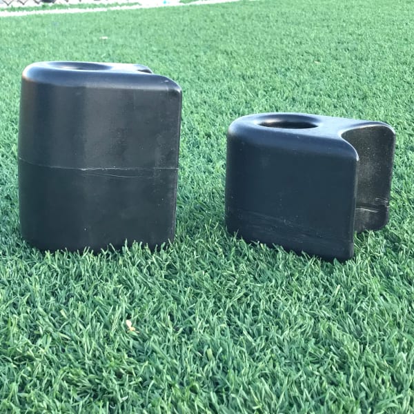 Two black plastic playground border filler end caps resting on artificial grass, designed for playground border openings.