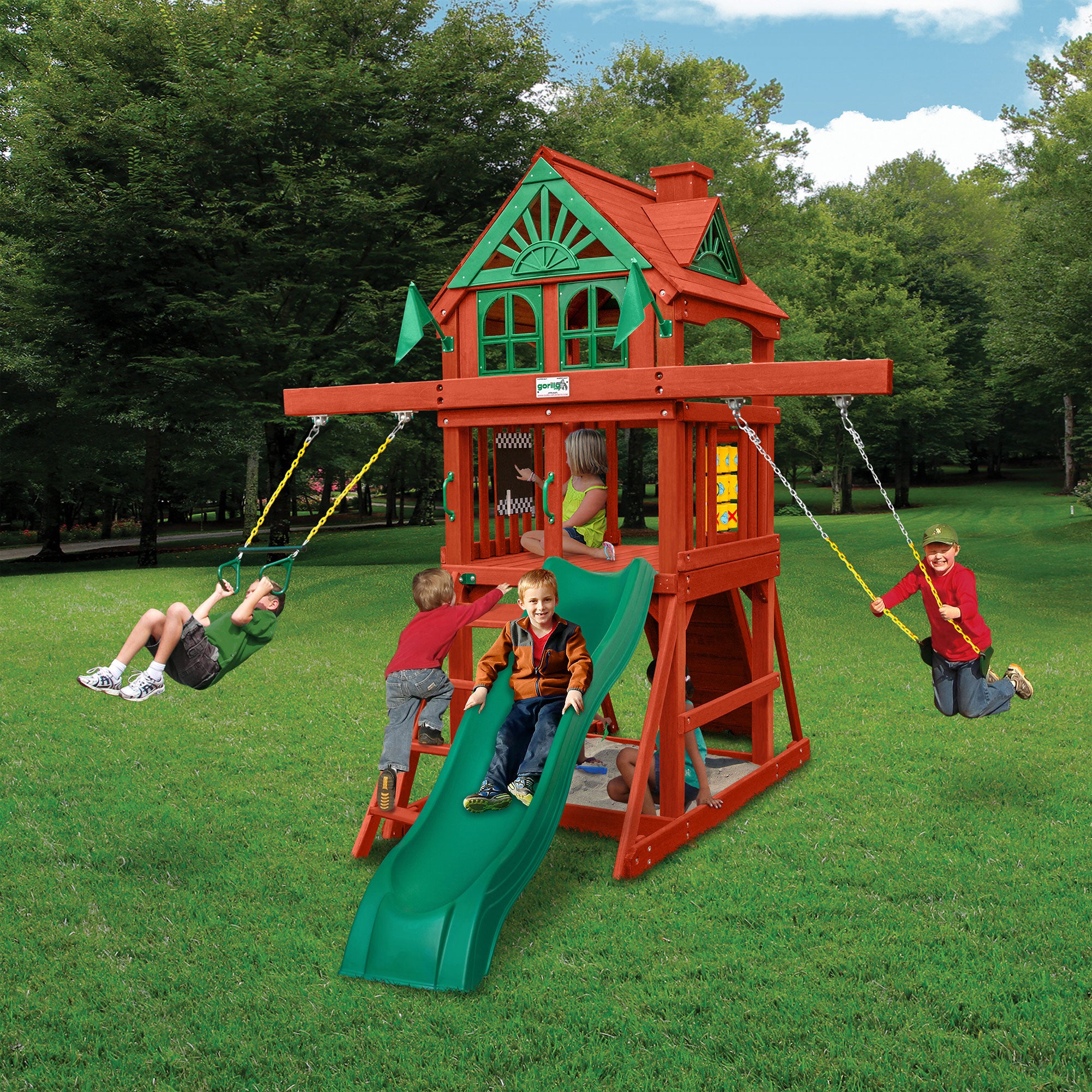Compact wooden playset with green slide, two yellow belt swings, tic-tac-toe panel, sandbox, and children playing outdoors
