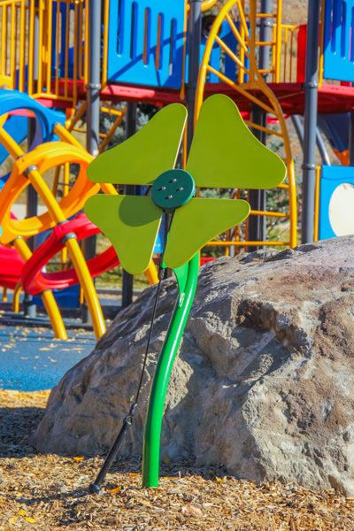 Green flower-shaped outdoor musical instrument with four petals and curved stem in colorful playground setting