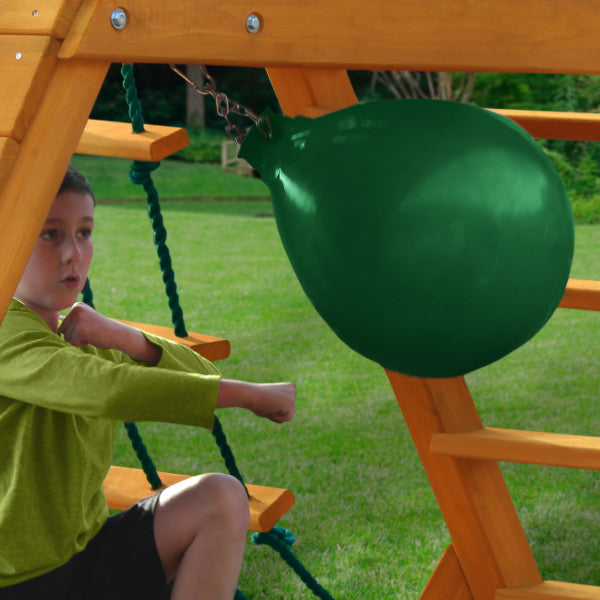 Child on wooden swing set with green punching ball, rope ladder, and grassy backyard setting