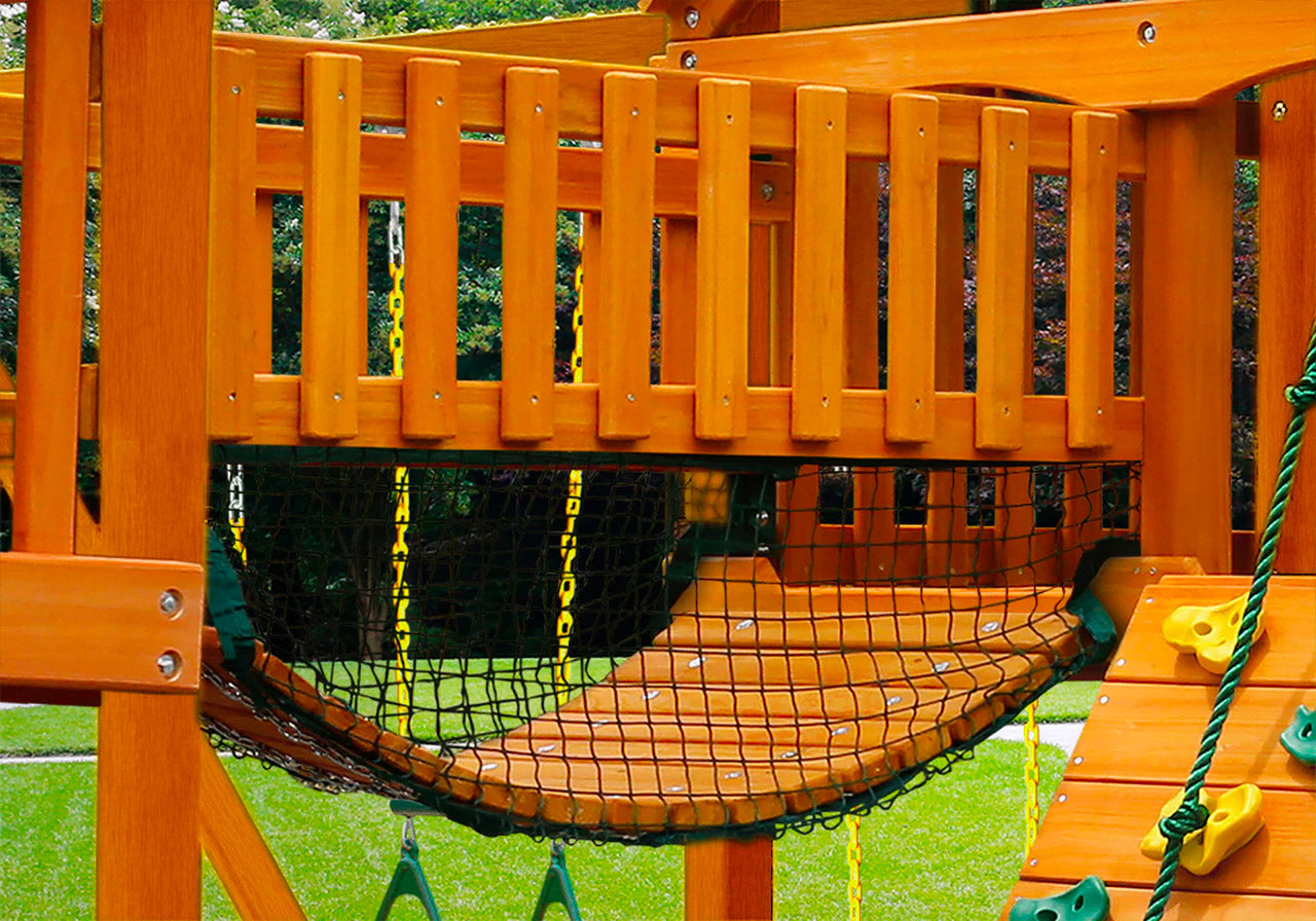Amber-stained wooden playset bridge with black safety netting, green climbing rope, and yellow climbing holds