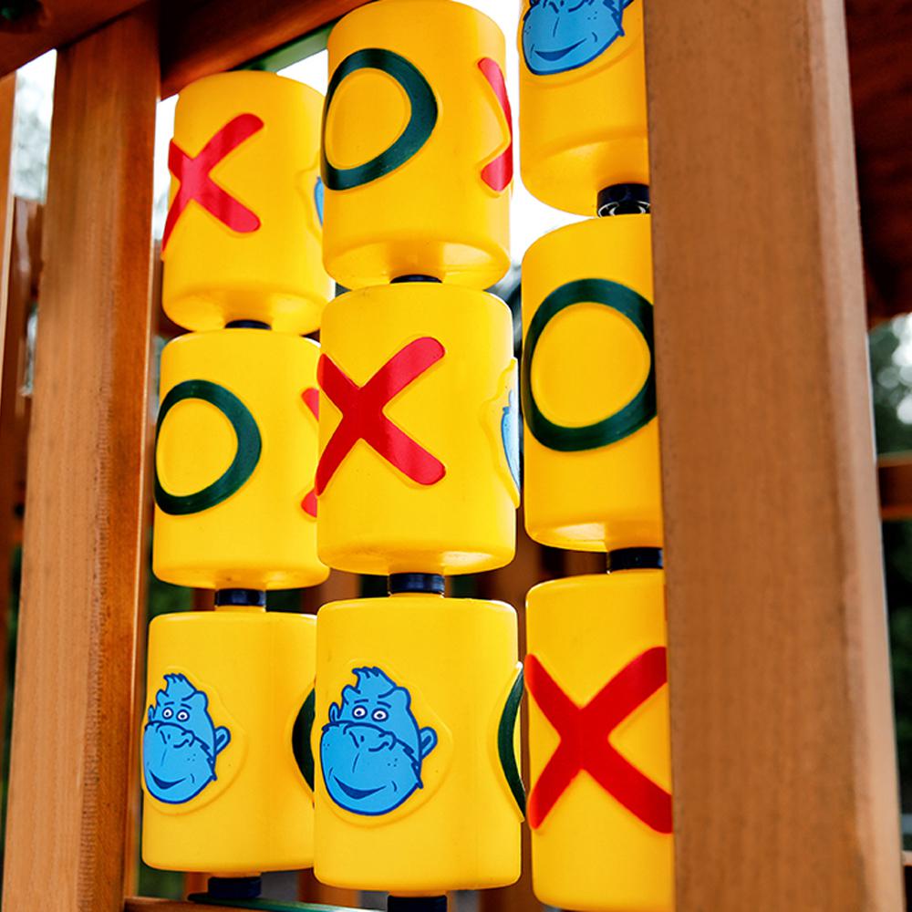 Yellow tic-tac-toe game panel with red Xs, green Os, and blue gorilla faces on wooden swing set play structure
