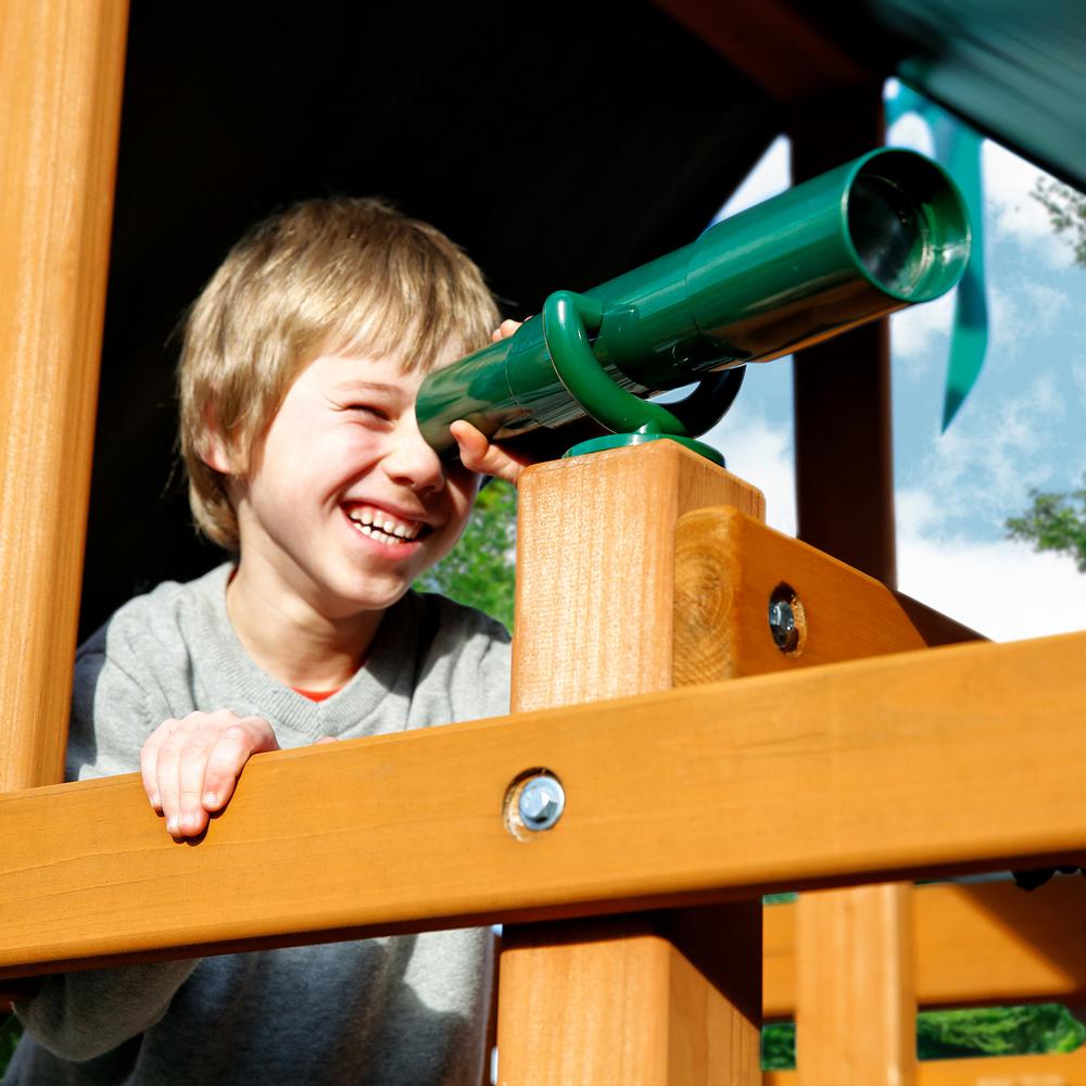 Child smiling through green telescope on amber-stained cedar wood playset deck with green vinyl canopy
