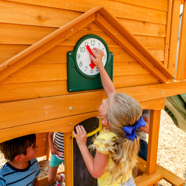 Child adjusting movable hands on play clock attached to wooden lower clubhouse of outdoor playset with nearby children