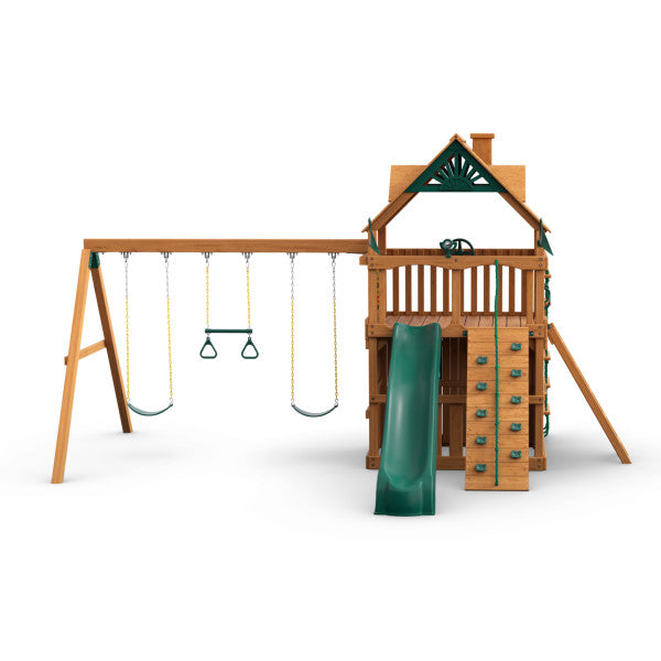 Wooden playset with amber finish featuring two belt swings, trapeze bar, green slide, rock climbing wall, and upper clubhouse with decorative roof
