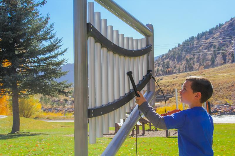 Child playing outdoor musical chime instrument with anodized aluminum tubes in a park setting