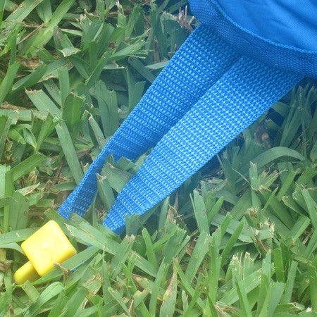 Blue nylon strap with yellow plastic stake securing inflatable sports bounce house on grass