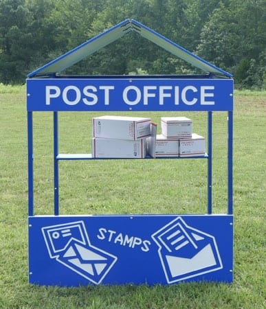 Blue children's playhouse with post office theme, featuring mail illustrations, stamps, and stacked mailboxes on a shelf