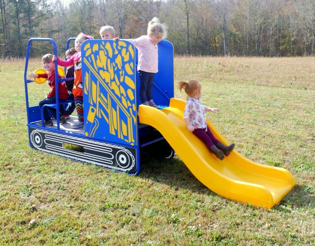 Children playing on a blue and yellow construction-themed playground slide with steering wheels on a grassy field
