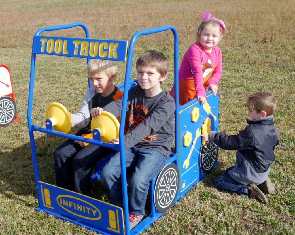 Blue outdoor play structure shaped like a tool truck with interactive panels and children playing around it