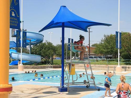 Lifeguard Shade Structure with blue canopy shading lifeguard chair at outdoor aquatic center pool