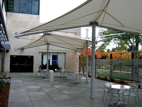 Single post shade structure with tensioned fabric top over outdoor metal tables and chairs on patio