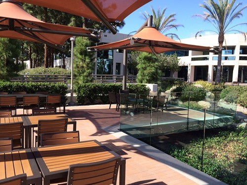 Modern rust-colored cantilever single post shade structure over outdoor seating near glass railing and landscaping