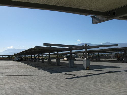 Double slanted cantilever shade structure with two columns and angled fabric canopy over paved area