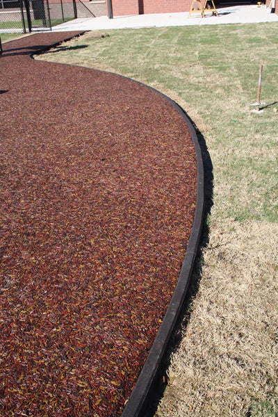 Curved black rubber playground border containing red recycled rubber mulch next to grassy area