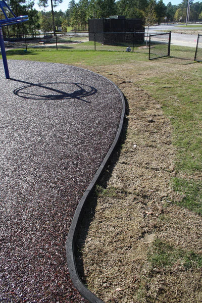 Curved molded rubber curb with built-in drainage containing loose fill surfacing at playground edge with basketball hoop shadow