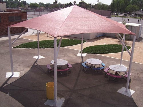 Hexagon Shade Structure with 6 Posts providing shade over outdoor picnic tables in a paved park area