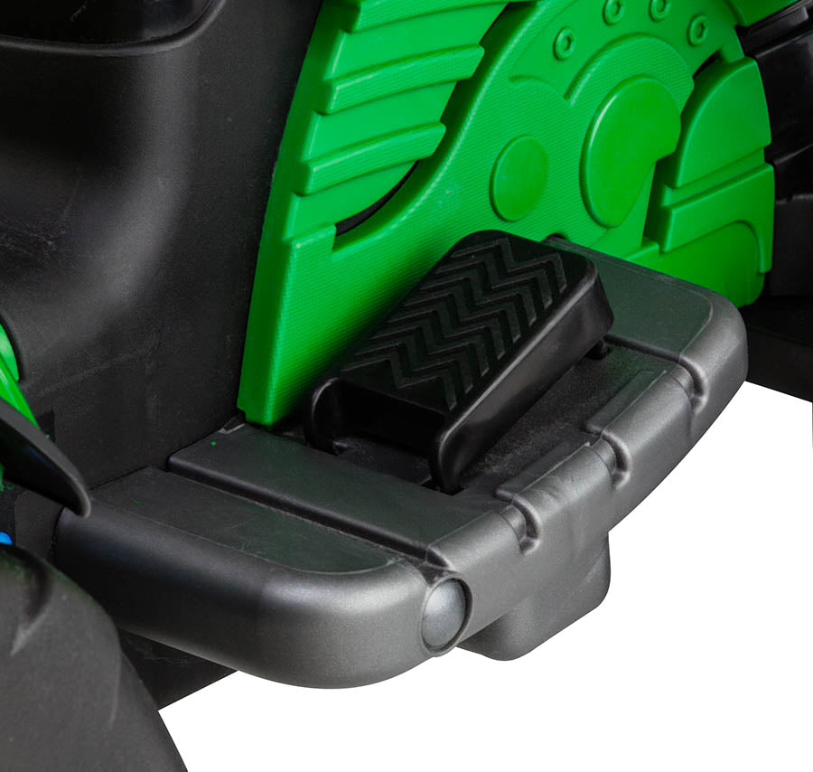 Black foot pedal on green and black children's ride-on construction vehicle with textured surface and raised edges