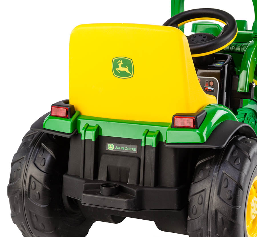 Green and yellow children's ride-on tractor with large black wheels, steering wheel, and front scoop bucket from rear view