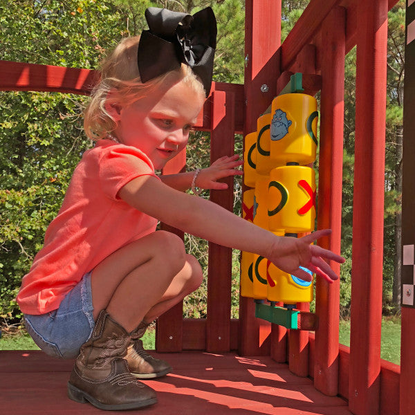 Young child playing with yellow tic-tac-toe panel on redwood wooden swing set deck outdoors