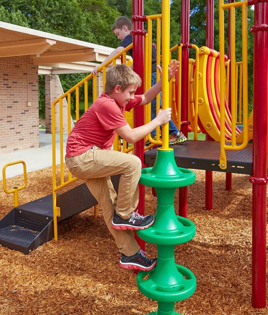 Child climbing green spiral climber on red and yellow playground structure with wood chip ground cover