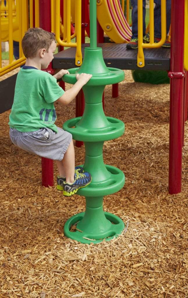 Child climbing green spiral climber on colorful playground structure with wood chip ground cover