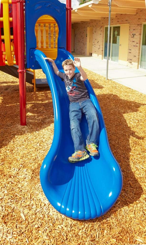 Child sliding down a bright blue curved slide on a colorful playground structure with red and yellow accents