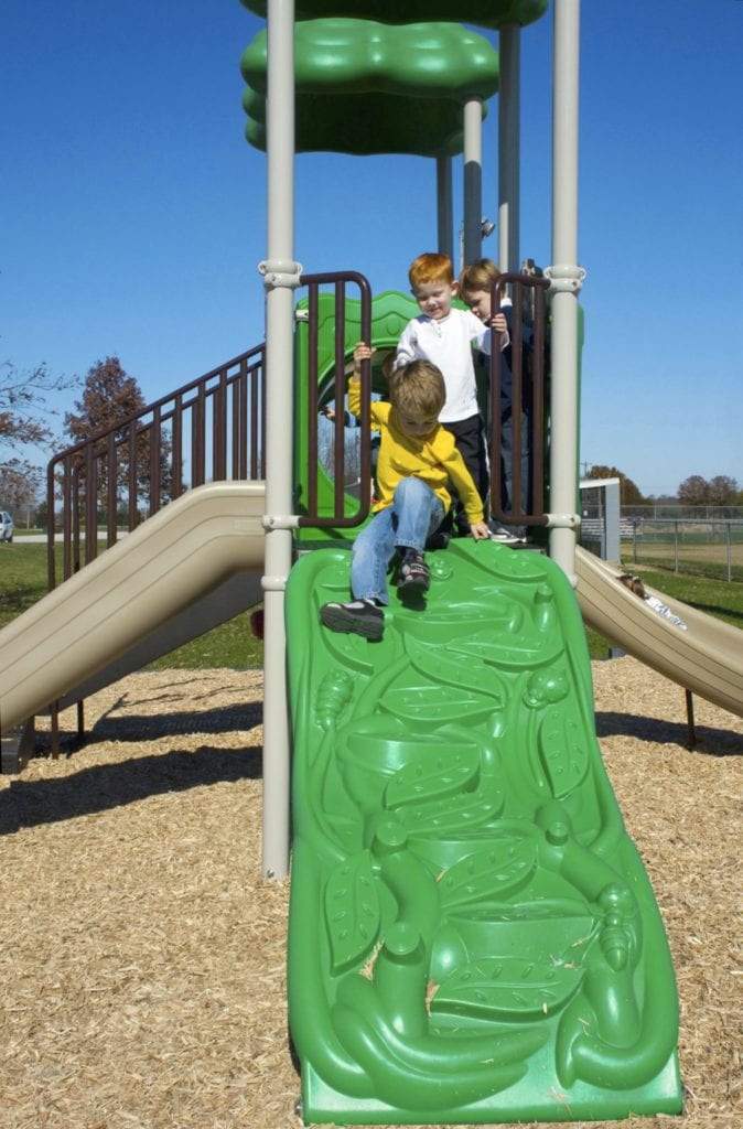 Children climbing on green nature-themed ramp and beige slides of a playground structure with spiral climber and interactive panels under clear sky