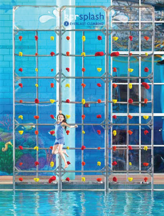 Kersplash Crystal Clear Pool Climbing Wall with red and yellow Groperz hand holds on stainless steel frame, child climbing above pool water