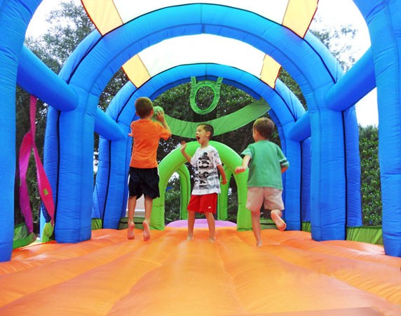 Three children playing inside a colorful inflatable sports bouncer with basketball hoops and soccer goals.