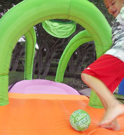 Inflatable sports bouncer with green arches, orange floor, purple goal areas, and a child kicking a green ball inside