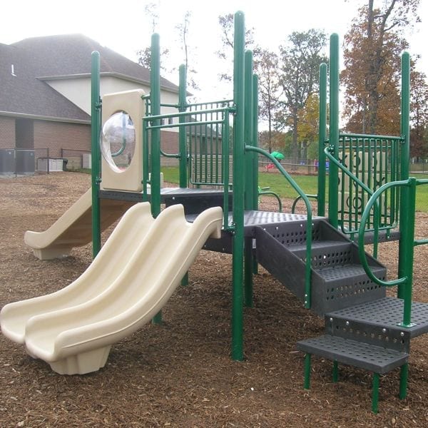 Playground with dual beige slides, green metal posts, stairs, climbing features, and wood chip ground surface.