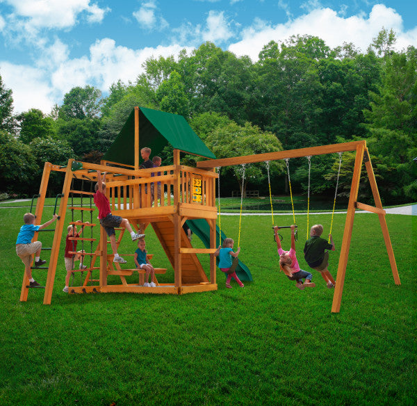Wooden playset with green vinyl canopy, climbing wall, rope ladder, slide, swings, and tic-tac-toe panel on grass