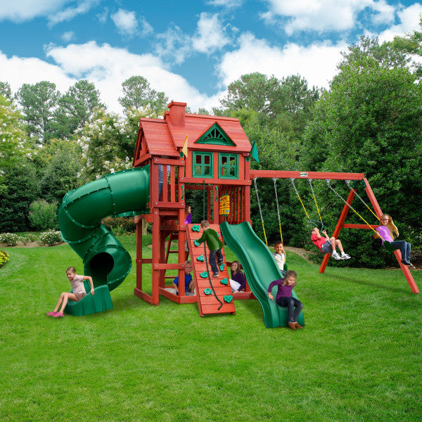 Cedar wood playset with two slides, rock climbing wall, swings, playhouse with windows and shutters on grass