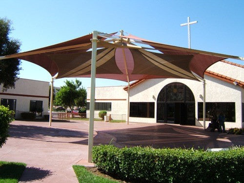 Hexagonal dual-layer fabric shade structure with six posts over paved courtyard near church building