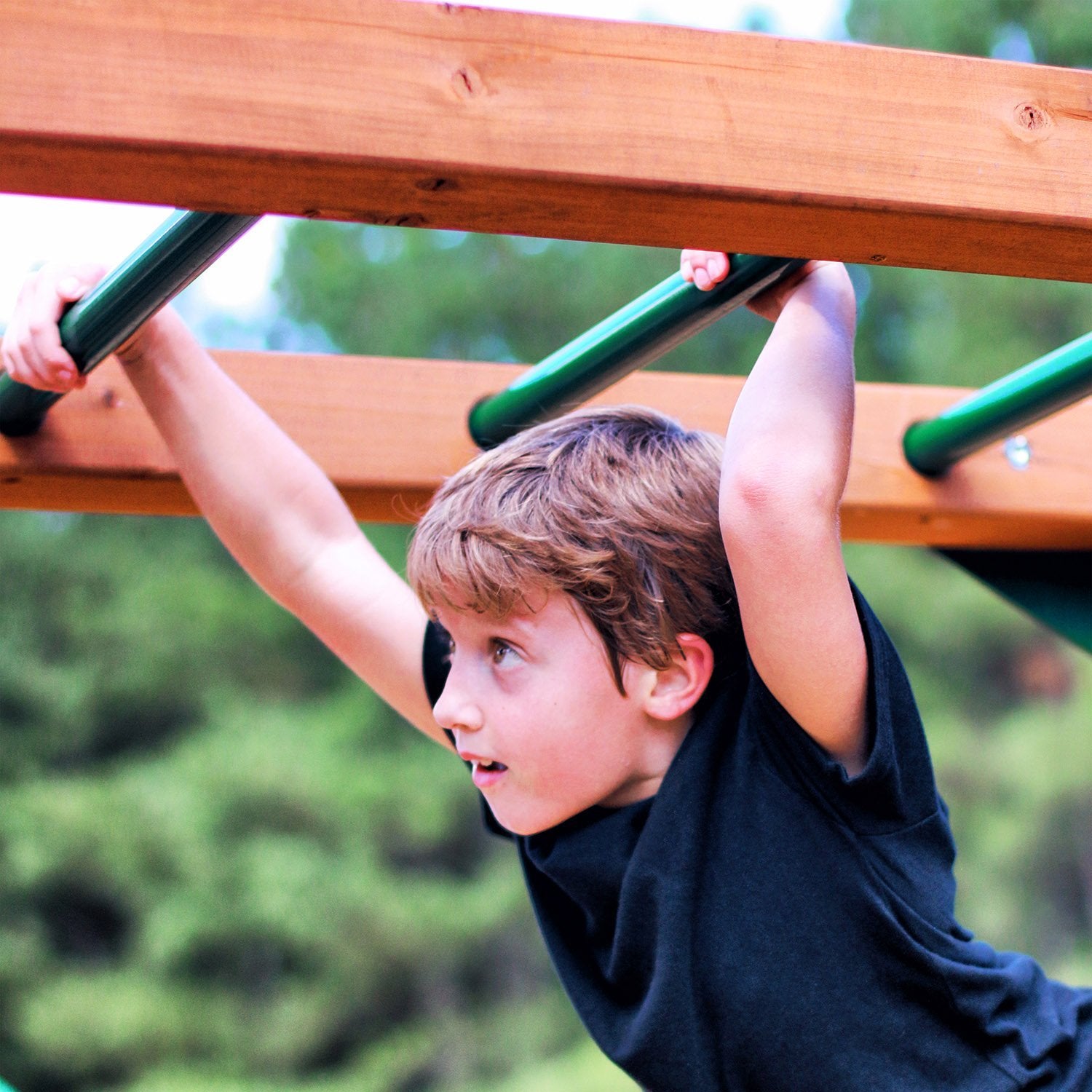 Child climbing wooden monkey bars with green metal rungs on outdoor cedar swing set in natural backyard setting