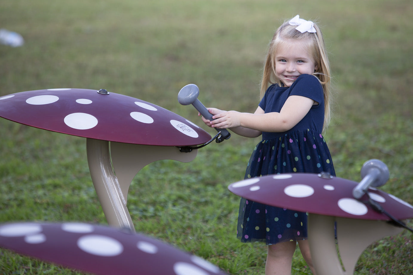 Child interacting with red mushroom-shaped outdoor musical instruments with white spots on green grass