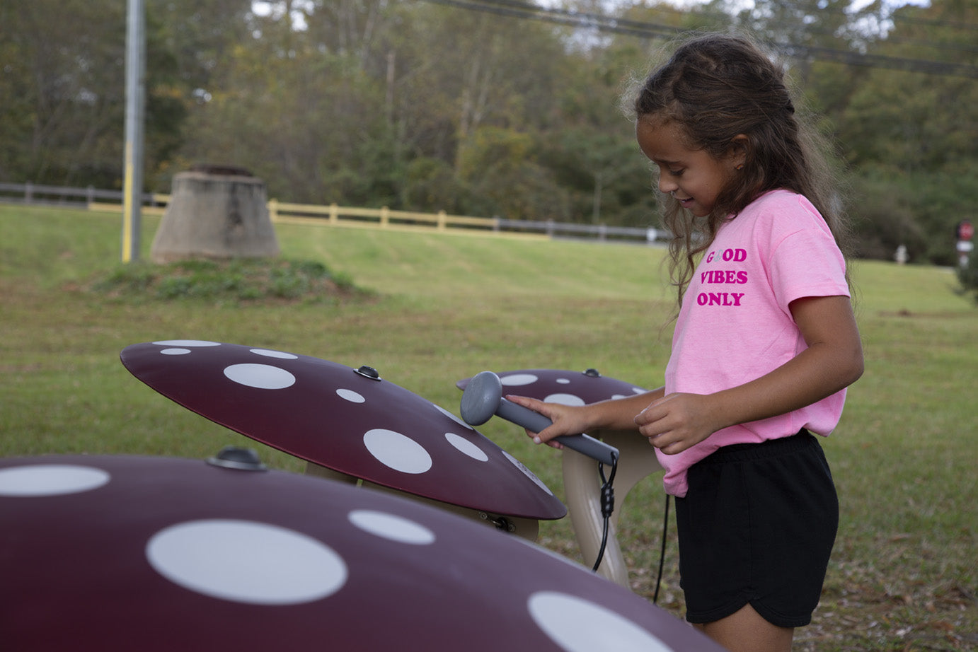 Child playing outdoor mushroom-shaped musical instruments with red caps and white spots in a grassy park setting