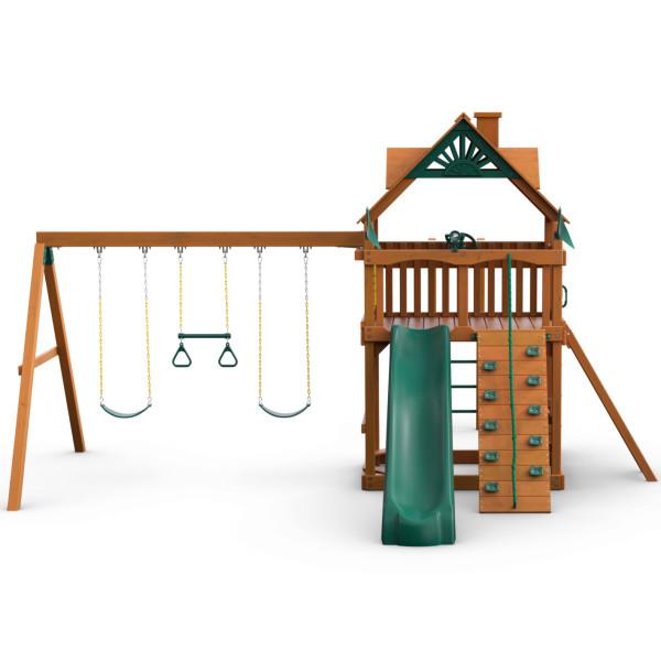 Wooden playset with amber finish featuring green slide, rock climbing wall, two belt swings, trapeze bar, and elevated platform with wood roof