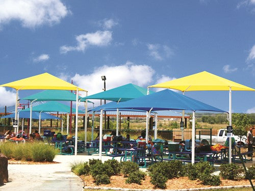Colorful pyramid-shaped shade structure with blue, green, and yellow fabric covering picnic tables in outdoor park setting
