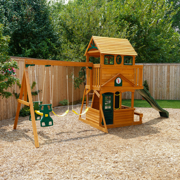 Ashberry Wooden Swing and Play Set with two-story clubhouse, rock wall, high rail wave slide, two belt swings, toddler swing, and shaded cafe table in backyard