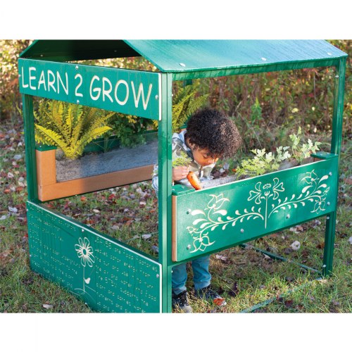 Green outdoor playhouse with clear root view planters, decorative floral panels, and a child interacting with plants.