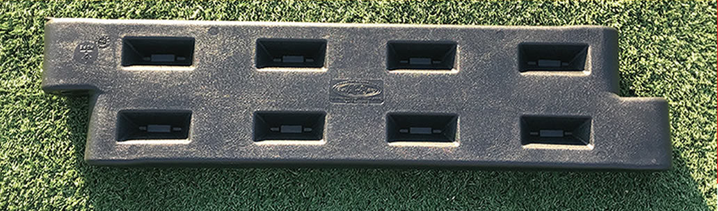 Black plastic playground border with textured surface, eight rectangular slots, and a spike on green turf